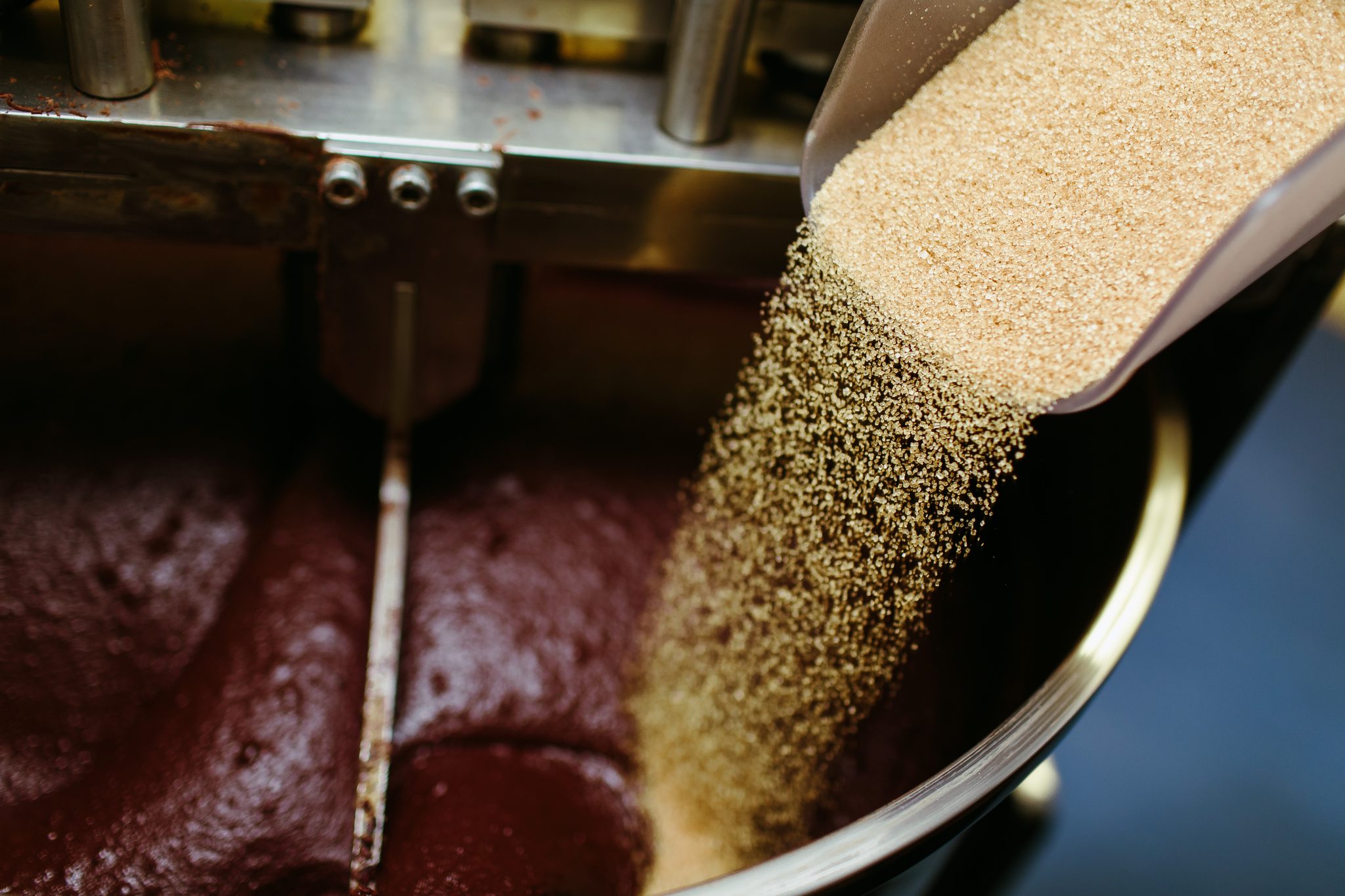 Artisan chocolate making, adding cane sugar to melanger